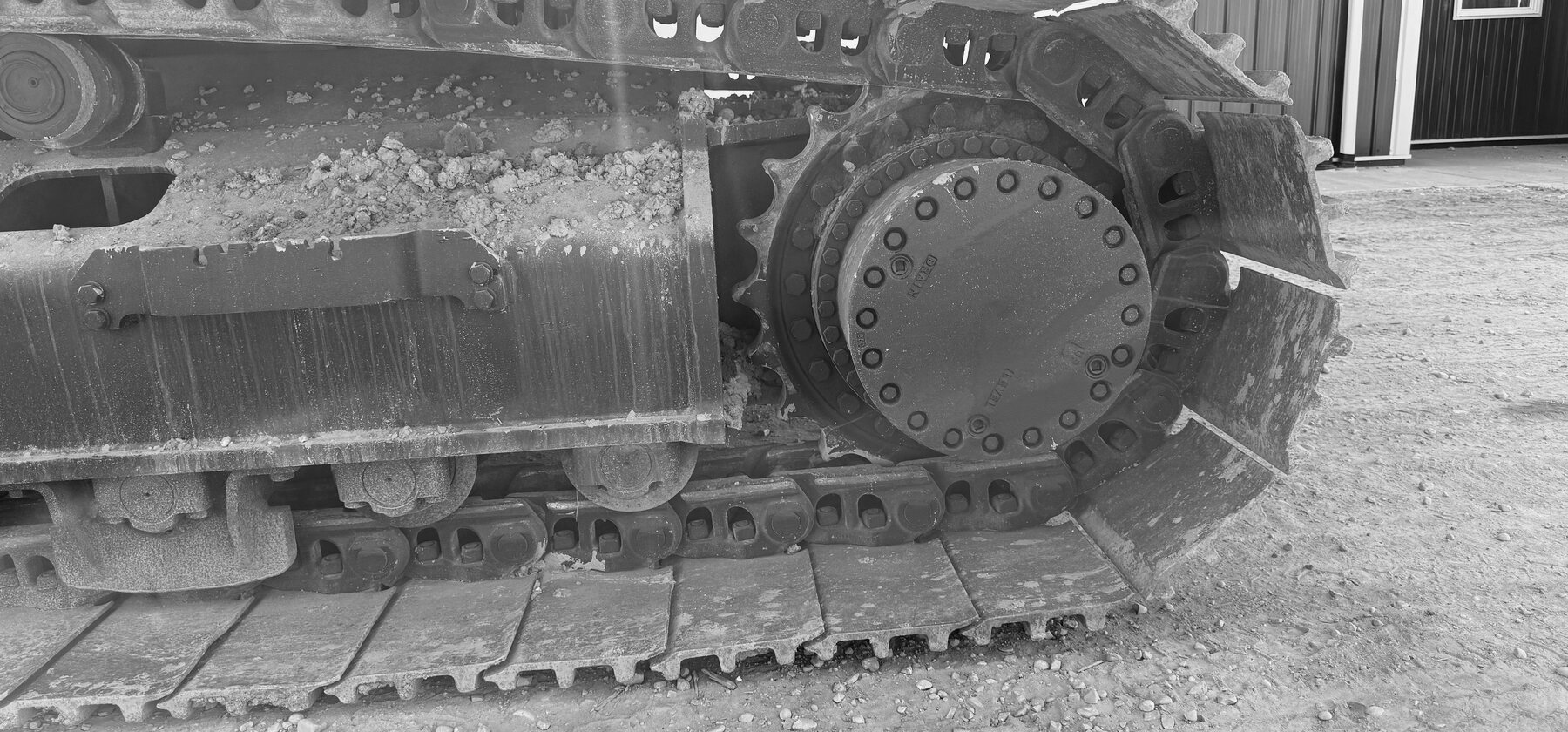 A final-drive hub and sprocket on an excavator undercarriage, packed with dried mud