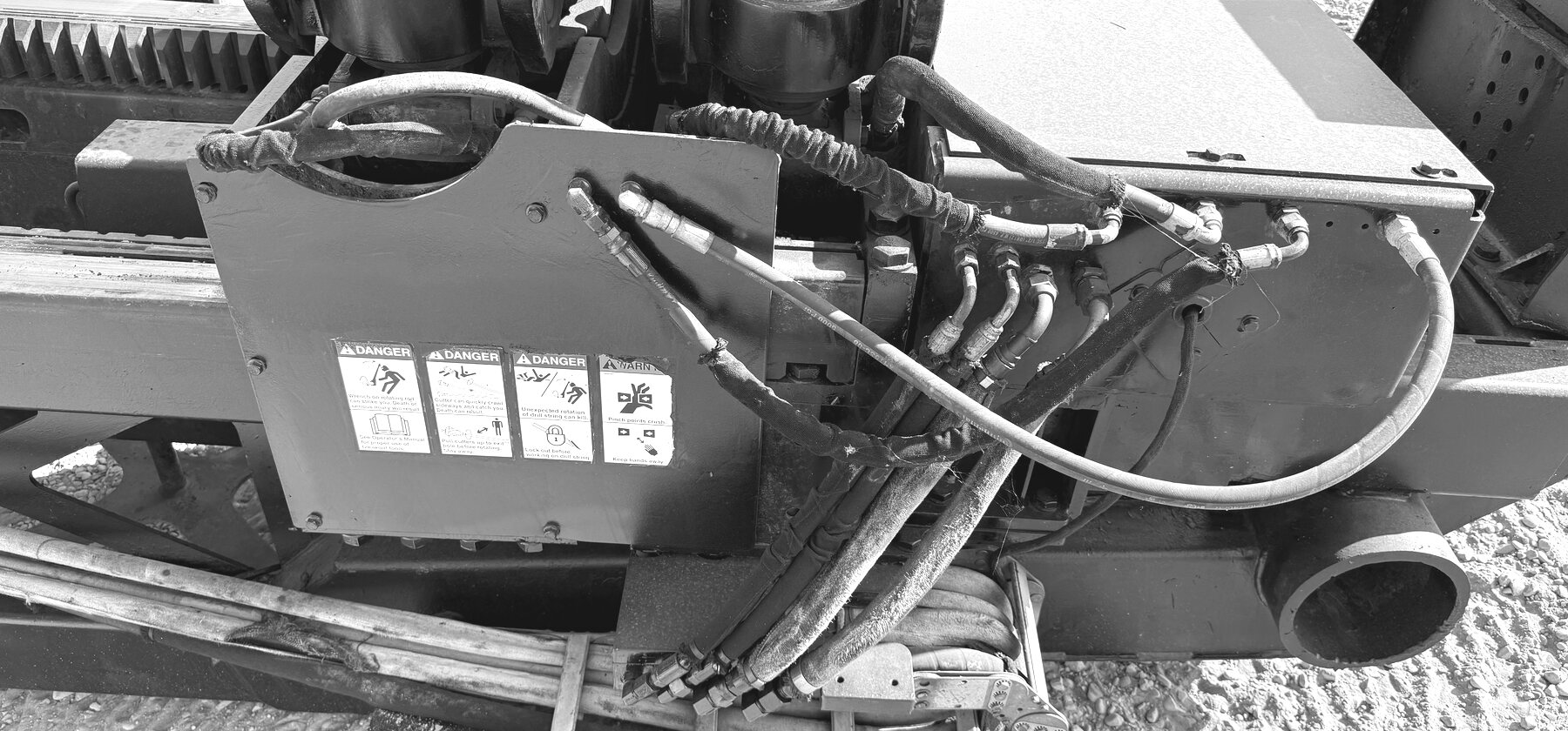 Coiled hydraulic hoses and rotating-equipment danger placards on a drill's gearbox housing