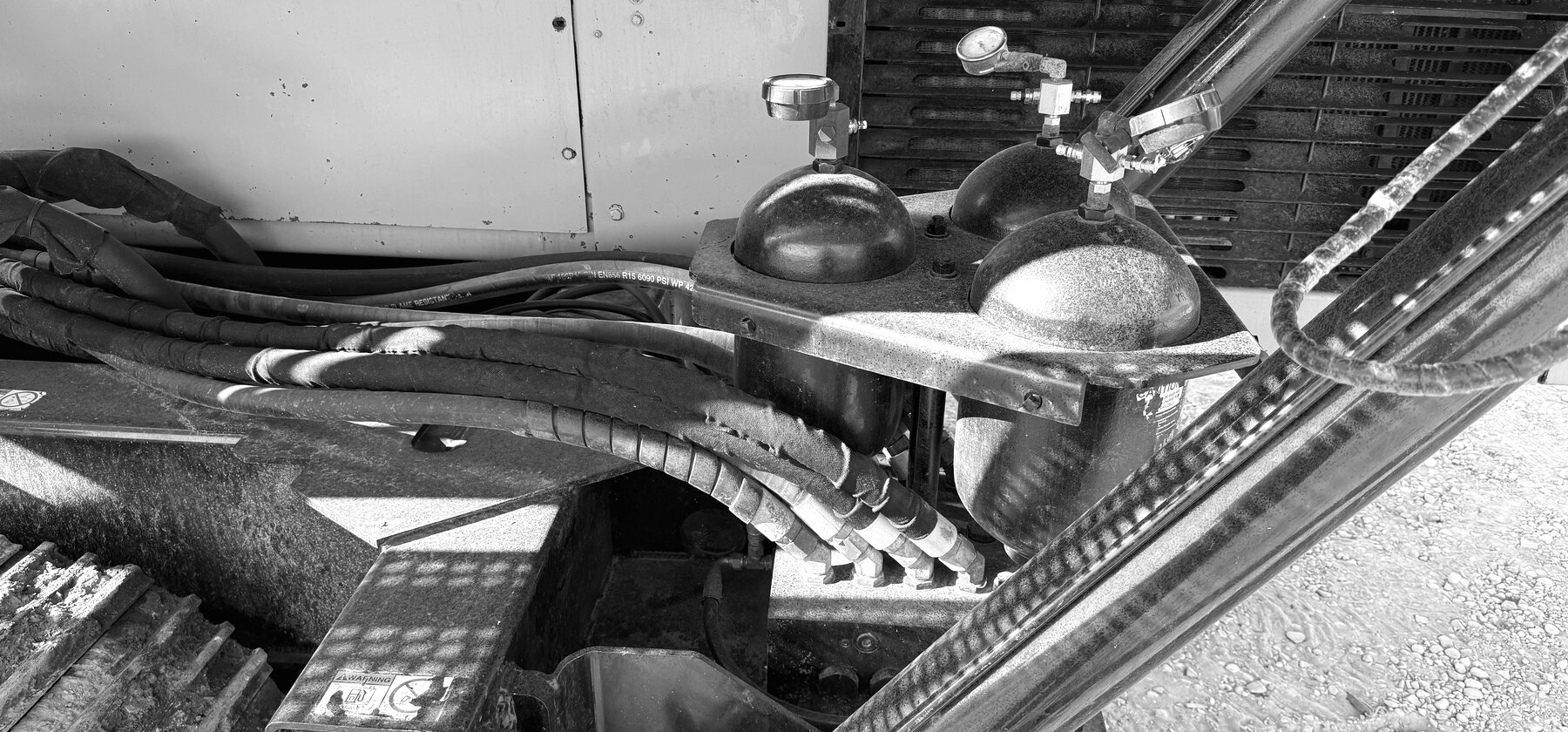 Pressure gauges and coiled hydraulic hoses on a drill rig's accumulator block beside its radiator