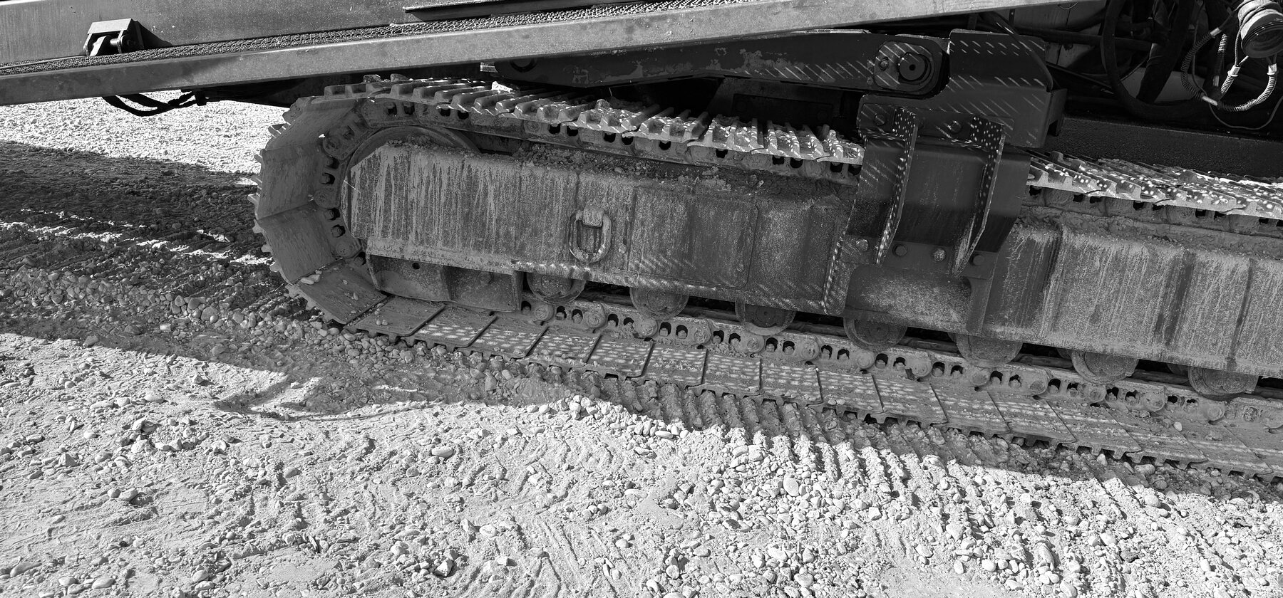 A dark track shoe and undercarriage frame with a diamond-plate access panel and lifting shackle
