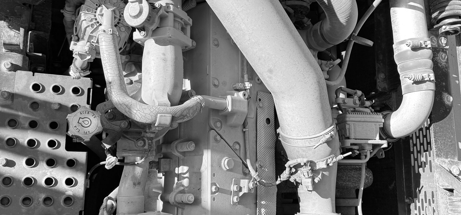 An oil filler cap and exhaust elbow with hose clamps inside an excavator engine bay