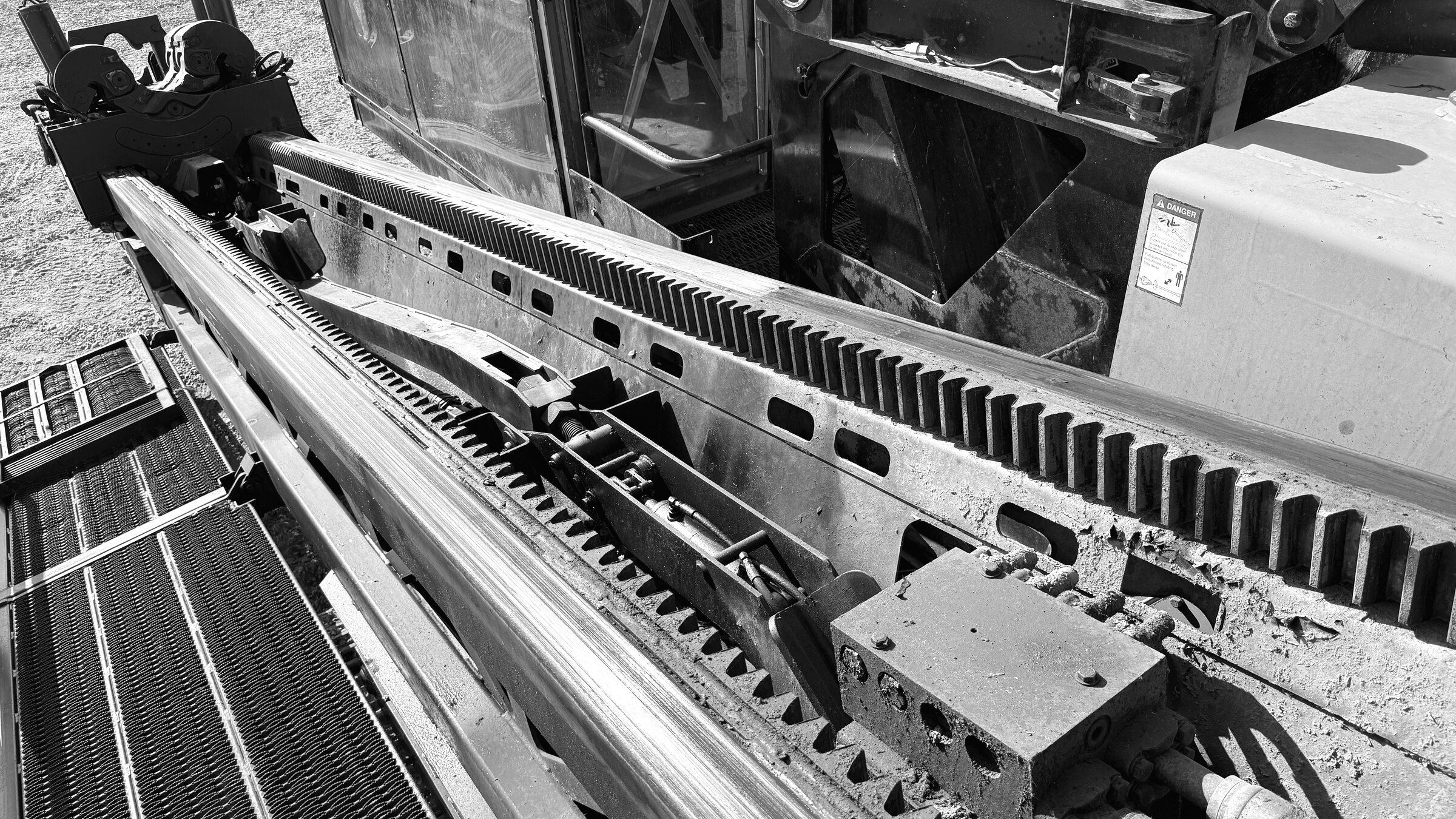 A drill rig's rod carriage and rack teeth, seen from above beside the open cab door