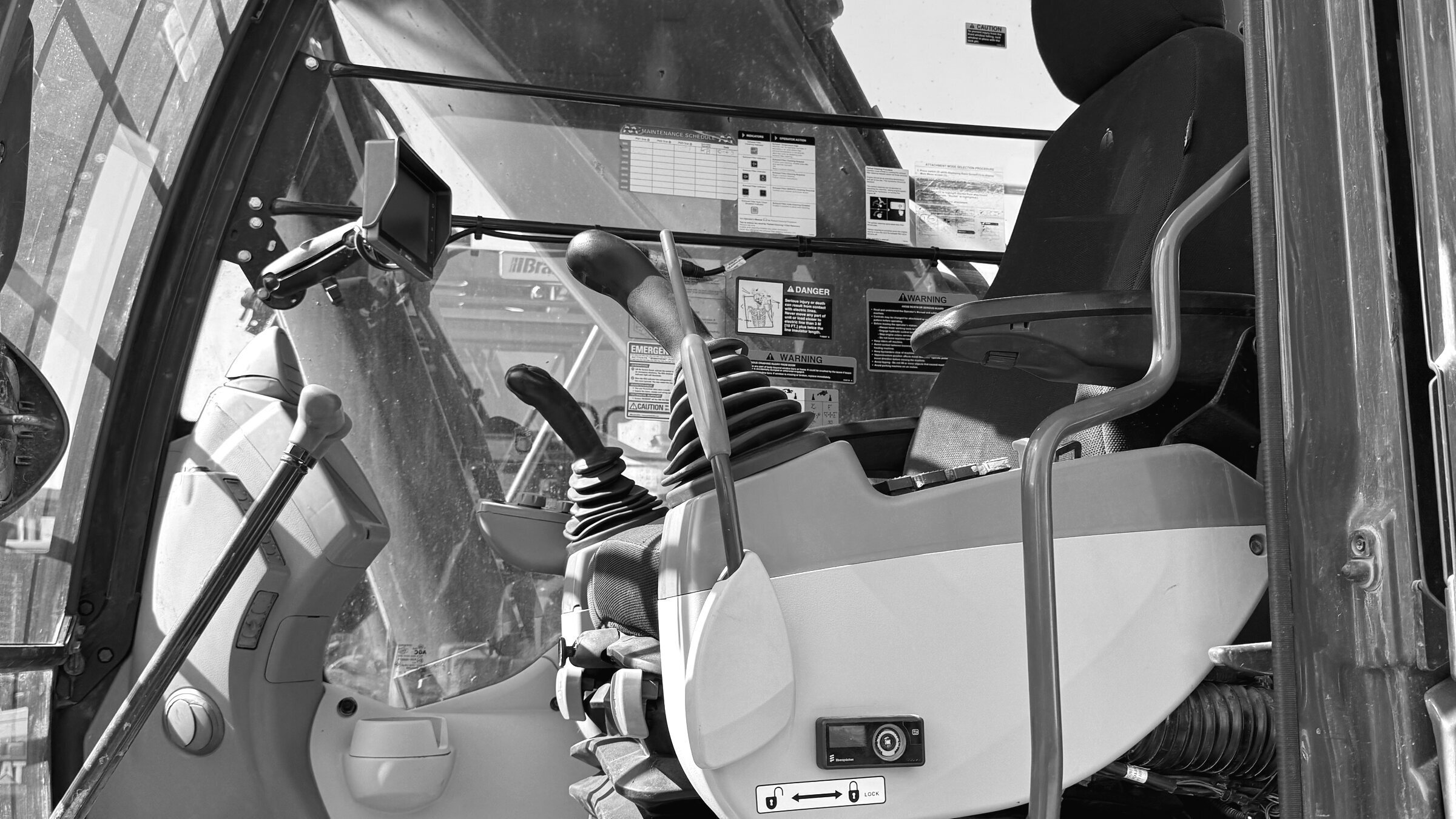 The inside of an excavator cab: both joysticks, the seat and the switch panel, seen from the doorway